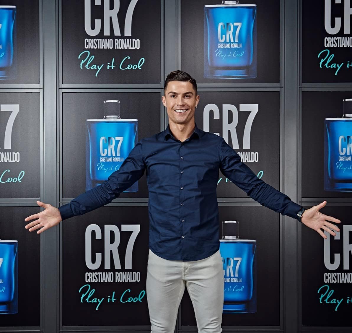 Man standing in front of a wall with arms out, showcasing CR7 Cristiano Ronaldo Play It Cool Eau De Toilette, a light and fresh fragrance for the active and energetic man. Ideal for everyday wear, this aromatic fragrance features herbal and citrus notes, capturing hearts with its delicate and sophisticated composition.