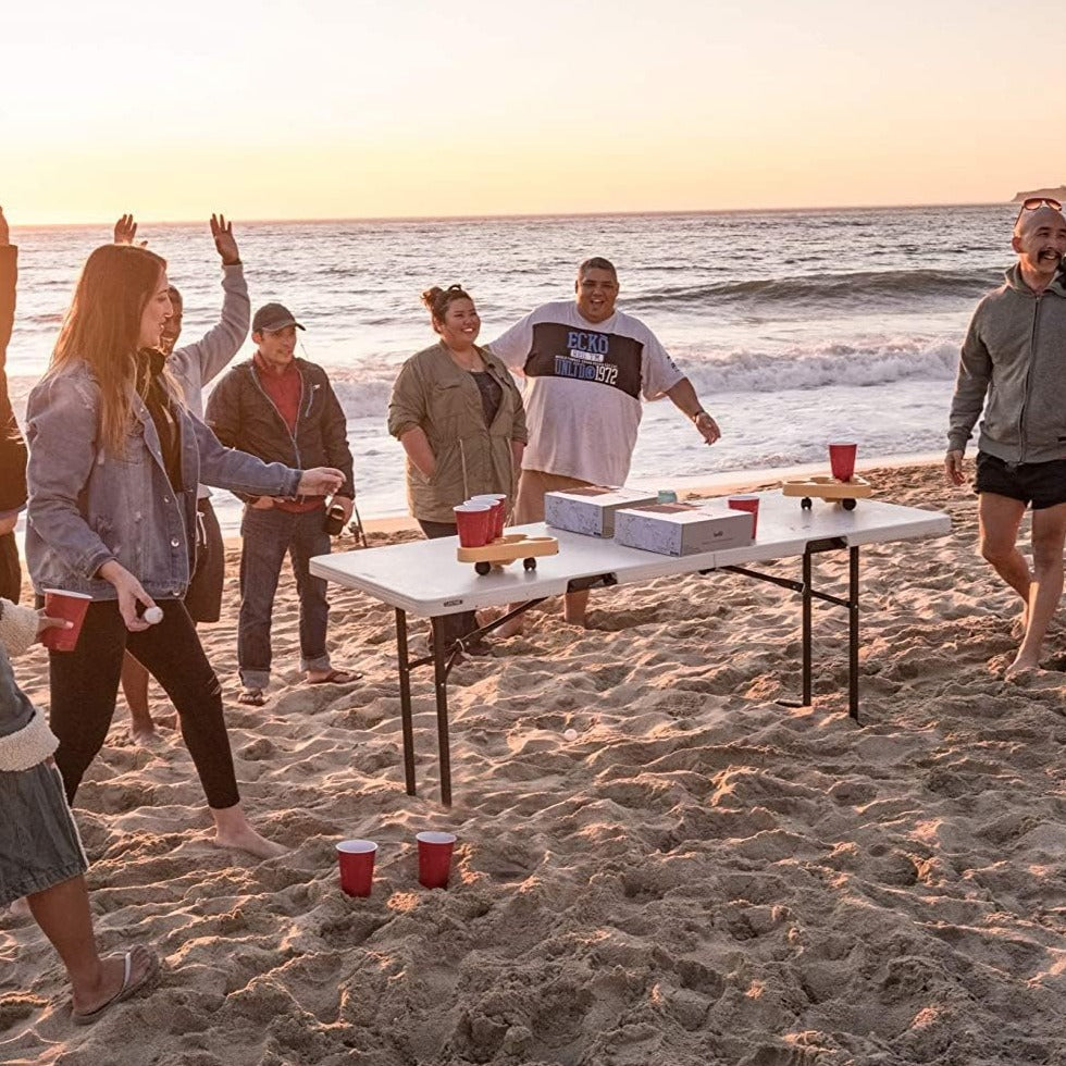 A group of people enjoying a beach party with the BRUU Moving Beer Pong Robot, a small robot that adds excitement to your beer pong games. The robot drives around the table, making the cups a moving target. With custom sensors, it ensures stability and avoids collisions. Spice up your traditional beer pong matches with this innovative addition. Each box contains 1 Robot, 2 Ping Pong Balls, and 1 Quick start guide. Let the good times roll!